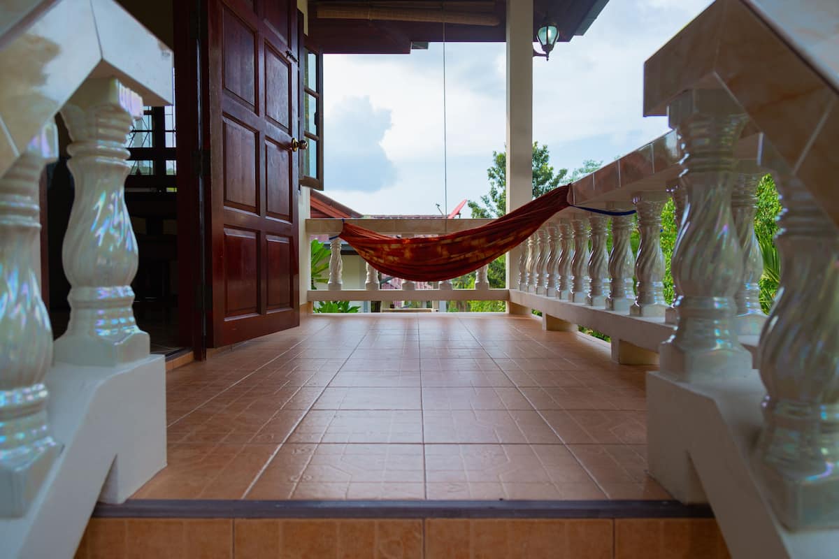 A tiled balcony with a hammock, white balustrades, and a wooden door.