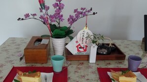 A table with two plates of cheesecake, a white ceramic pot, a wooden box, a blue mug, and a purple mug. - Traditional Arts Country Inn (Wujie)