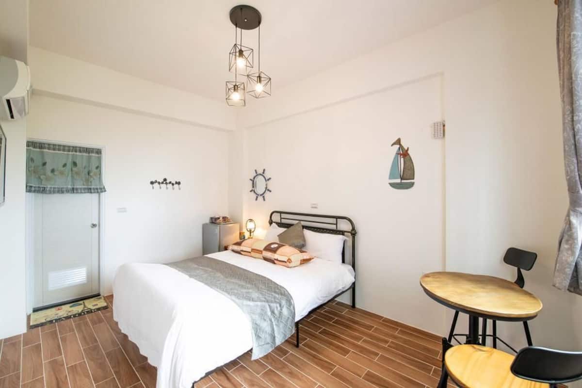 A bedroom with a bed, bedside table, lamp, and a small round table with a chair.