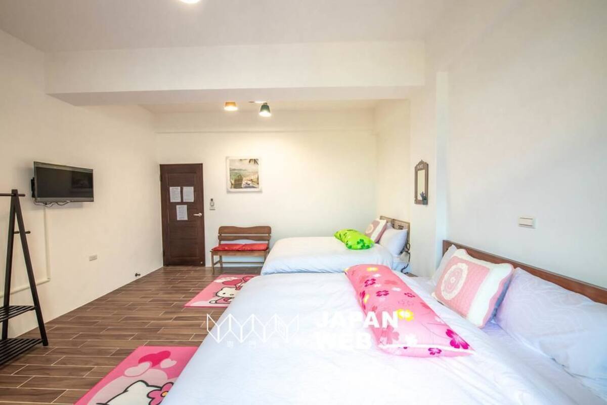 A bedroom with two beds, a TV, a wooden bench, and a door.