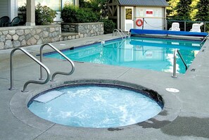 Ein Schwimmbecken mit Whirlpool, Steinmauern und einem Rettungsschwimmerstand.