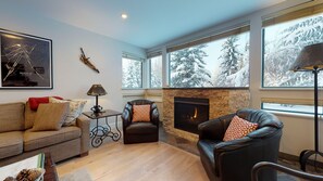 Una sala de estar moderna con chimenea, ventanas amplias con vistas nevadas, un sofá y un sillón de cuero.