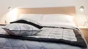 Ein ordentlich bezogenes Bett mit einer gesteppten Decke, zwei Nachttischlampen und einem Nachttisch mit Schublade.