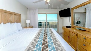A hotel room with a bed, a wooden dresser, a television, and a balcony with a view. - Seagull 202 - Quiet Beachfront Hideaway with Endless Ocean Views, Swimming Pool, Spa, Washer/Dryer (South Padre Island)
