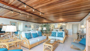 A spacious living area with a high wooden ceiling, wicker furniture, and a central seating arrangement. - Seagull 202 - Quiet Beachfront Hideaway with Endless Ocean Views, Swimming Pool, Spa, Washer/Dryer (South Padre Island)