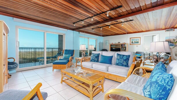 A spacious living room with a wooden ceiling, large windows, and a balcony. - Seagull 202 - Quiet Beachfront Hideaway with Endless Ocean Views, Swimming Pool, Spa, Washer/Dryer (South Padre Island)
