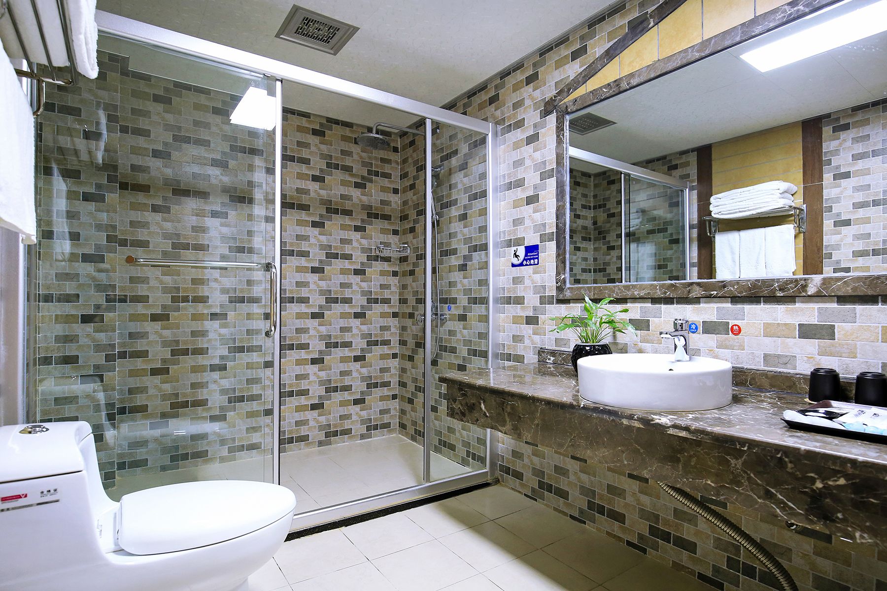 A modern bathroom with a glass-enclosed shower, a white toilet, a sink with a marble countertop, and a mirror above the sink.