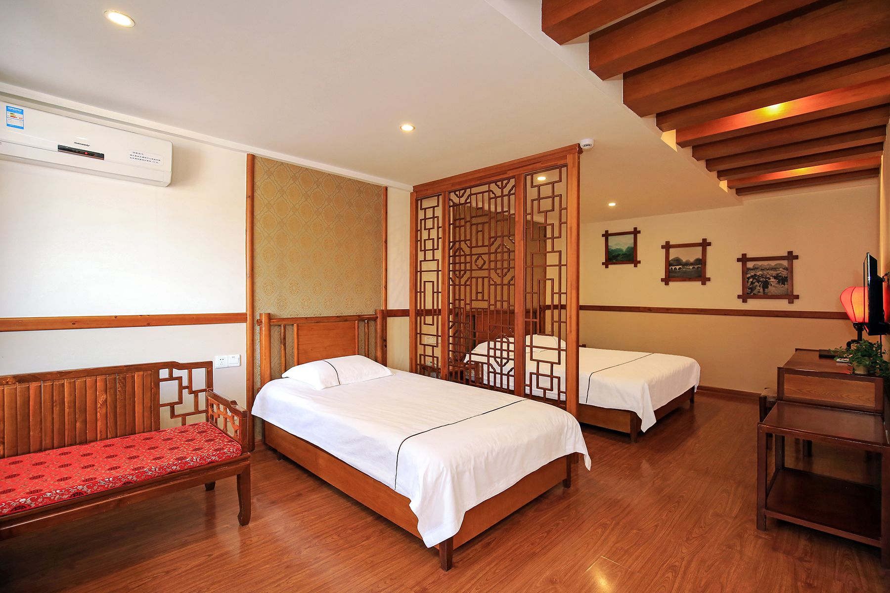 A hotel room with two beds, a wooden bench, a desk, and a traditional wooden screen.