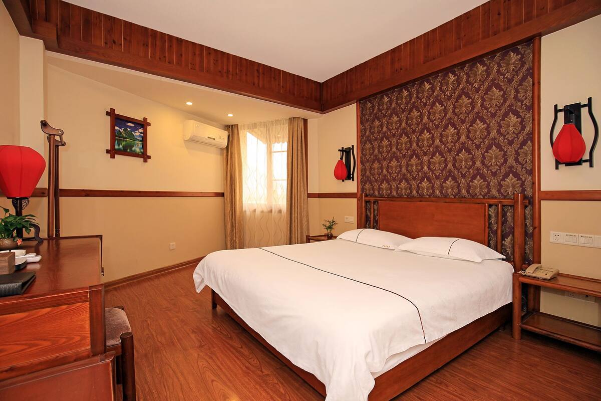 A hotel room with a wooden bed, a desk with a lamp, and a patterned wallpaper.