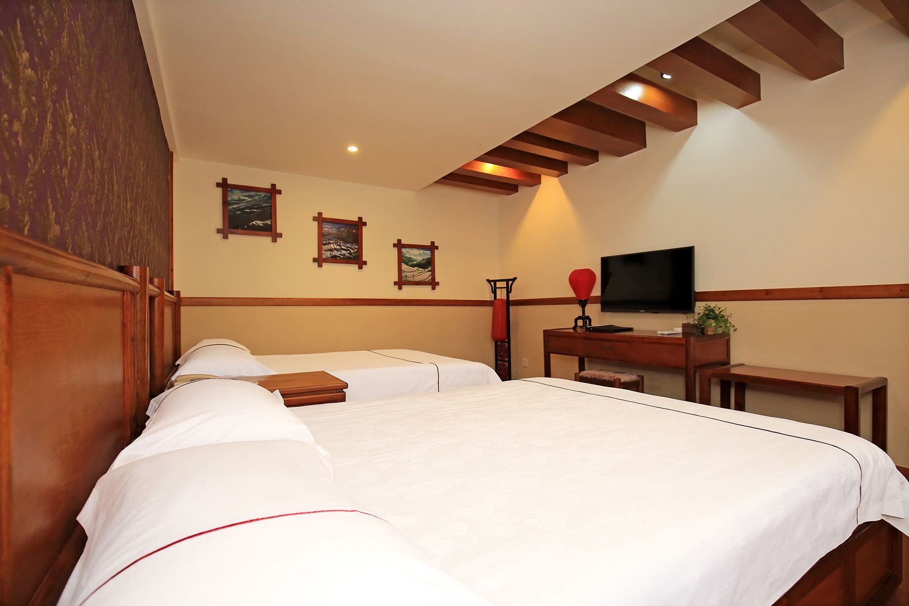 Quarto de hotel com uma cama grande, uma escrivaninha com televisão e três quadros na parede.