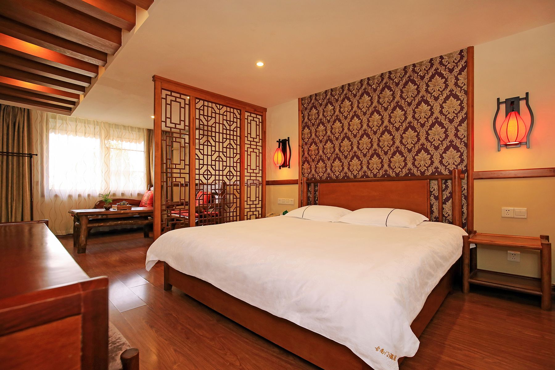 Una habitación de hotel con una cama grande, muebles de madera, un separador decorativo y adornos tradicionales en la pared.