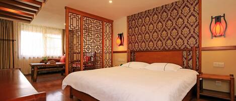 Una habitación de hotel con una cama grande, muebles de madera, un separador decorativo y adornos tradicionales en la pared.