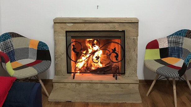 Un salon avec une cheminée, deux fauteuils à motifs et une horloge murale.
