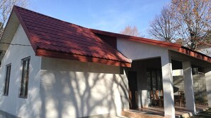 Une maison de plain-pied avec un toit recouvert de tuiles rouges, une véranda abritée avec des chaises et un petit jardin devant.