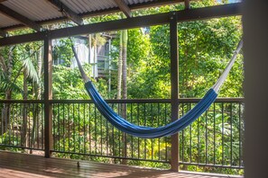 A hammock on a wooden deck with a view of lush greenery and a metal railing. - The Treehouse (Airlie Beach)