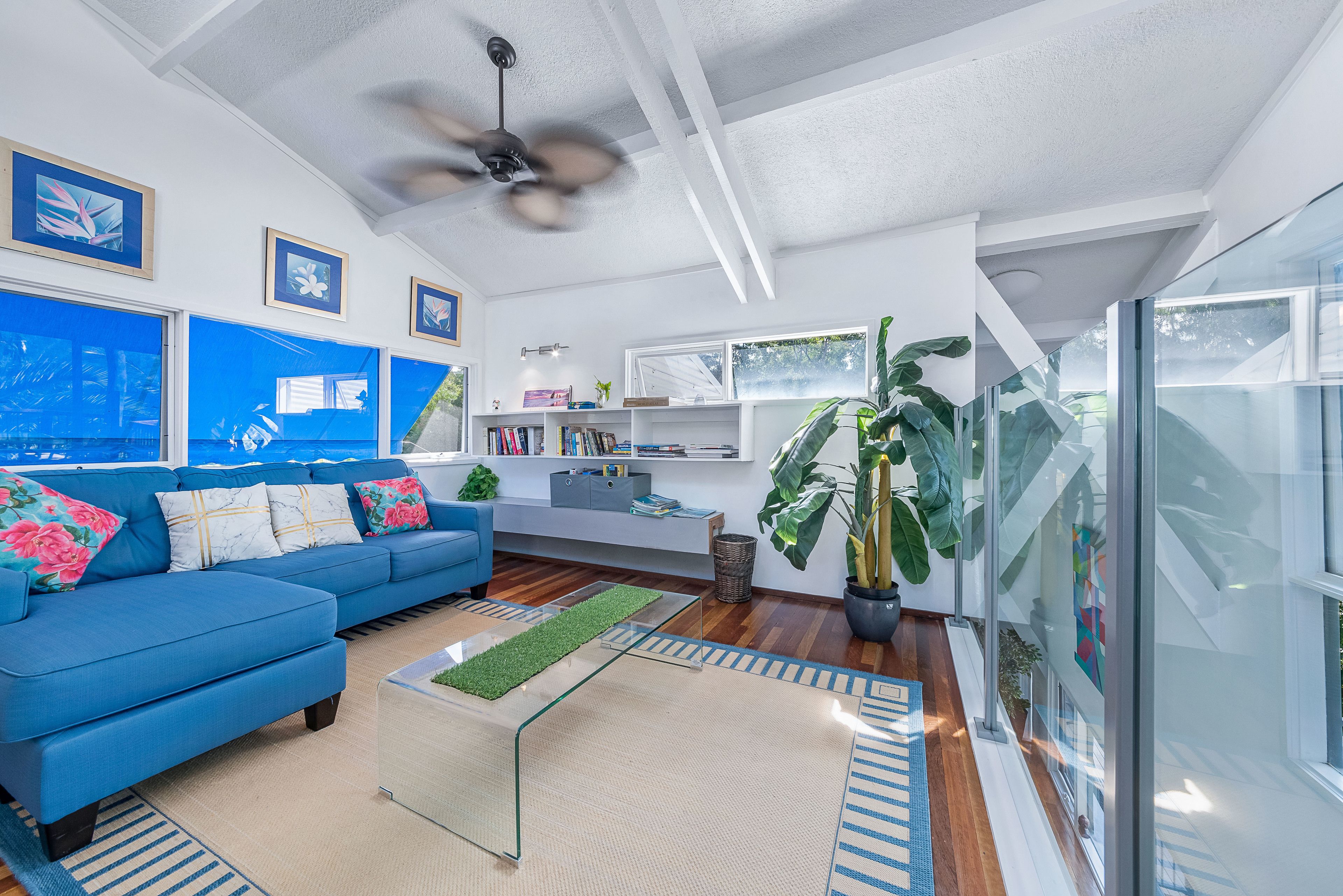 Un salon moderne avec un canapé bleu, un ventilateur de plafond et une grande fenêtre.