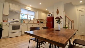 Une cuisine avec des meubles blancs, un réfrigérateur rouge, une table à manger en bois et un vase rempli de fleurs.