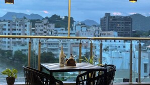 Una mesa con sillas y una botella en un balcón con vista a un paisaje urbano que incluye edificios y montañas.