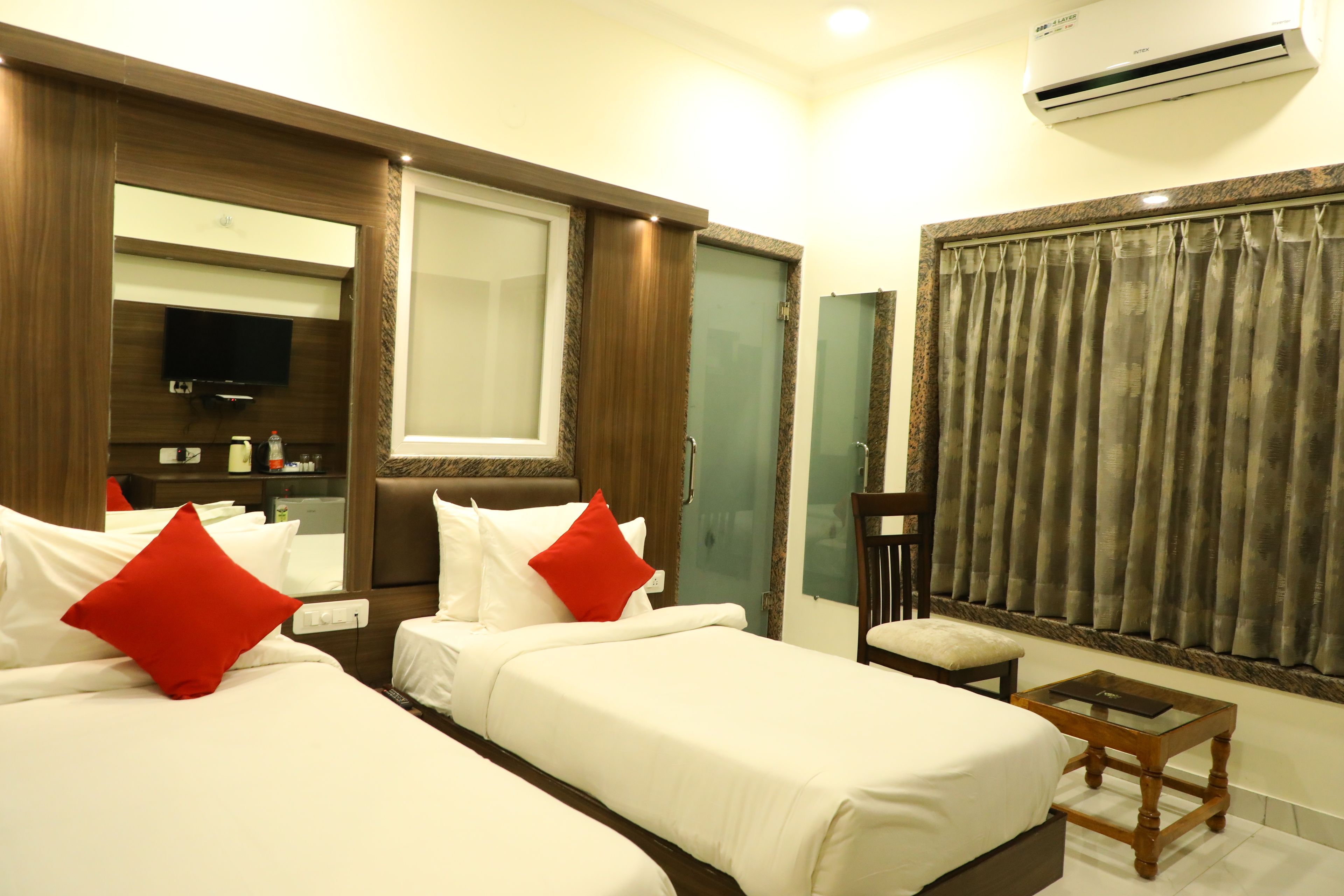 A hotel room with two beds, a TV, a small table, and a window with curtains.