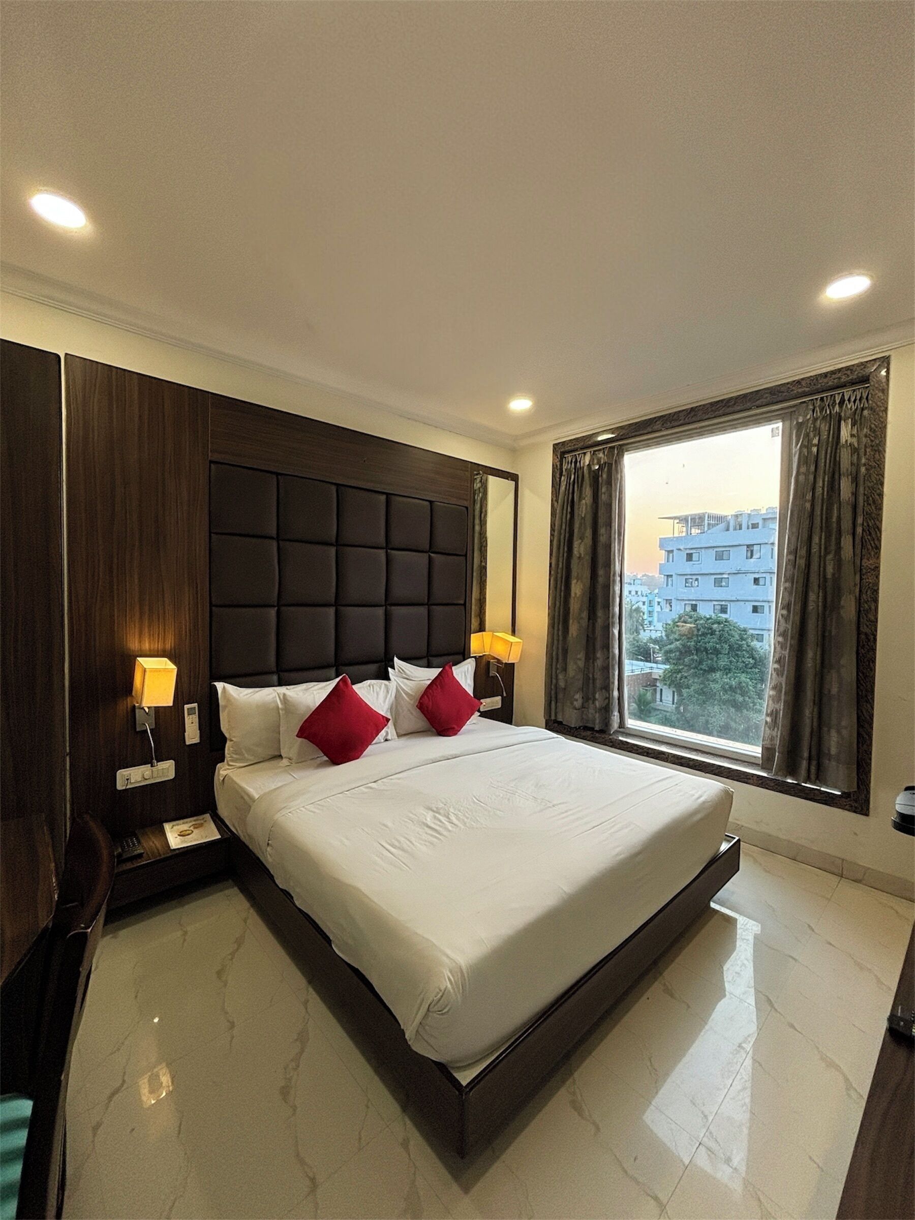 A hotel room with a large bed, two bedside lamps, a nightstand, and a window with curtains.