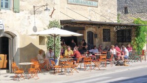 An outdoor cafe with tables and chairs, a sign reading "CAFE de la PLACE", and a rustic stone building in the background. - Stunning home in Saint-Rémy-de-Provence (Saint-Rémy-de-Provence)