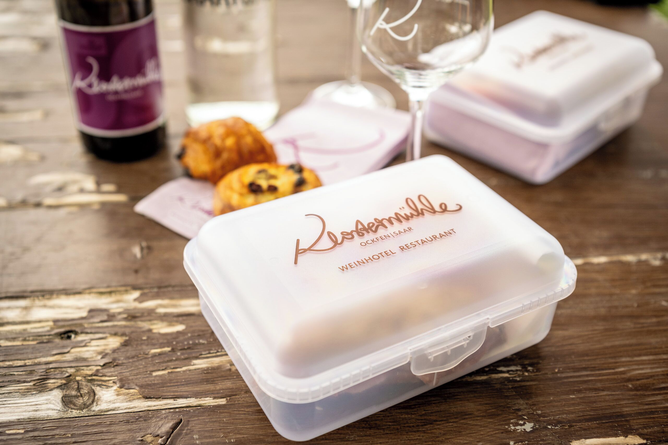A plastic container with a lid labeled "Klosterbrie" and "Weinhotel Restaurant" on a wooden table.