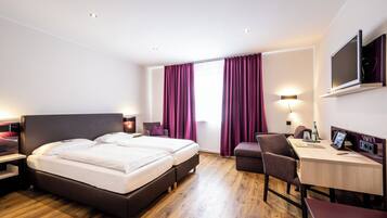 A hotel room with a double bed, a desk, a chair, and a TV.