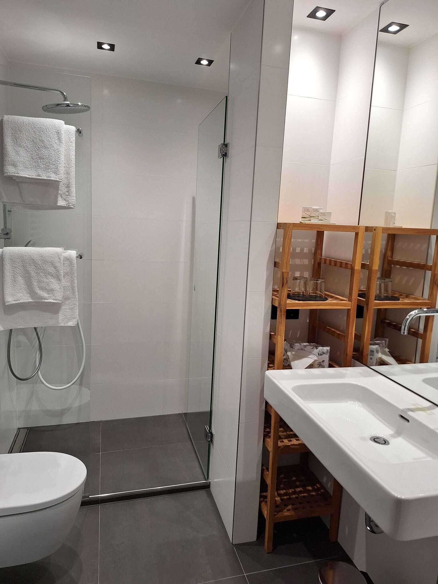 Une salle de bain moderne avec une douche à parois de verre, un lavabo blanc et une étagère en bois.