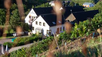 Ein weißes Gebäude mit Balkon, umgeben von Grünpflanzen und einem geparkten Auto.