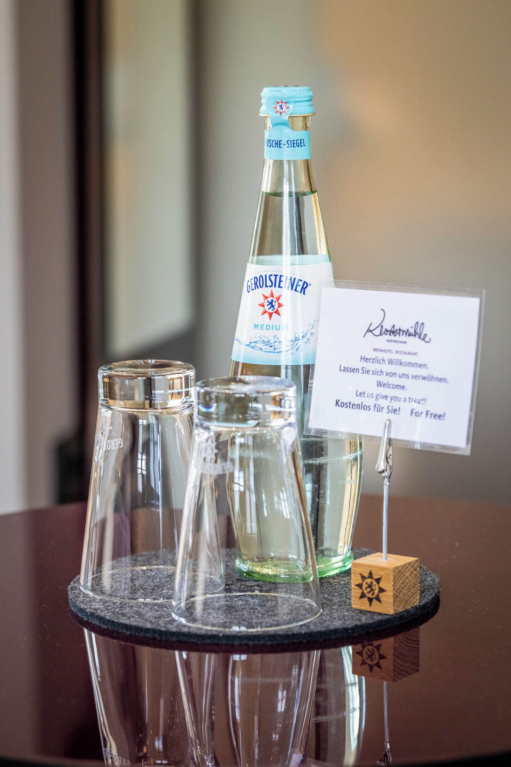 Una mesa con una botella de agua, un vaso y un cartel.