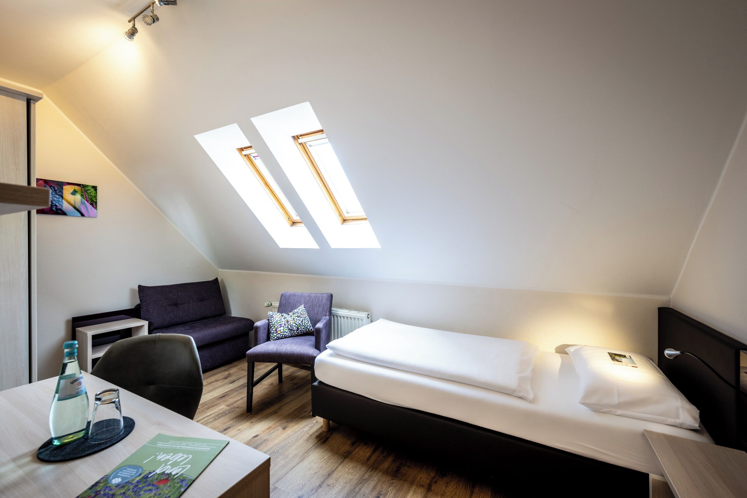 Una habitación pequeña y moderna con una cama, una silla, una mesa y un ventanal.