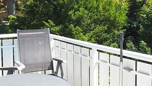 Een terras met een ronde tafel en twee stoelen, een wit metalen hek en een metalen paal met een camera.