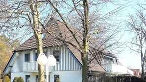 Een huis met twee verdiepingen, een schuin dak, een balkon en een verzorgd gazon.