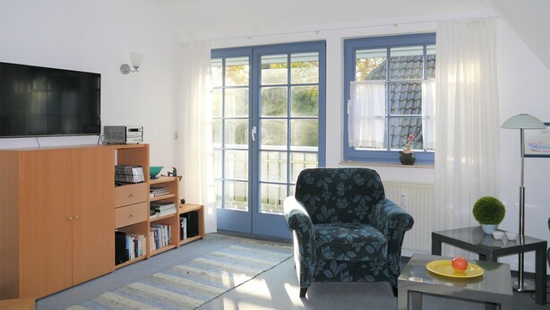 Een woonkamer met een televisie, een boekenkast, een fauteuil en een raam met gordijnen.