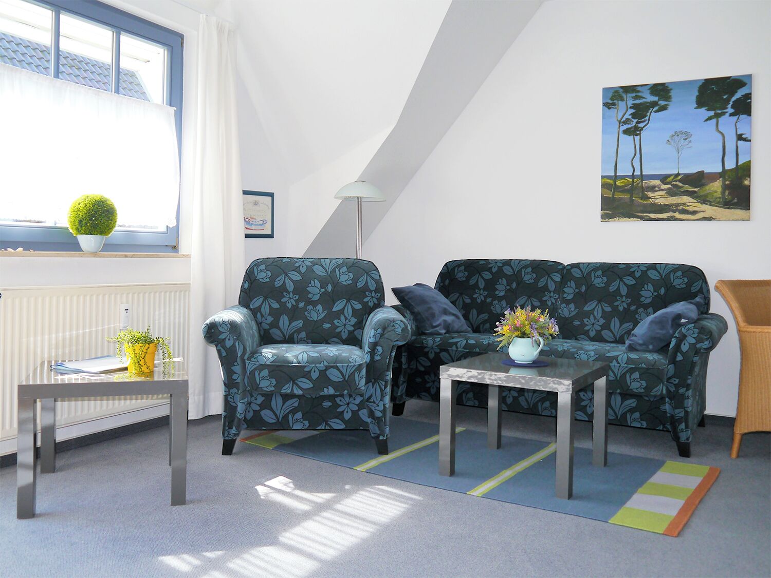 Ein gemütliches Wohnzimmer mit einer Couch, einem Sessel und einem kleinen Tisch mit einer Vase.