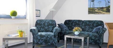 Ein gemütliches Wohnzimmer mit einer Couch, einem Sessel und einem kleinen Tisch mit einer Vase.