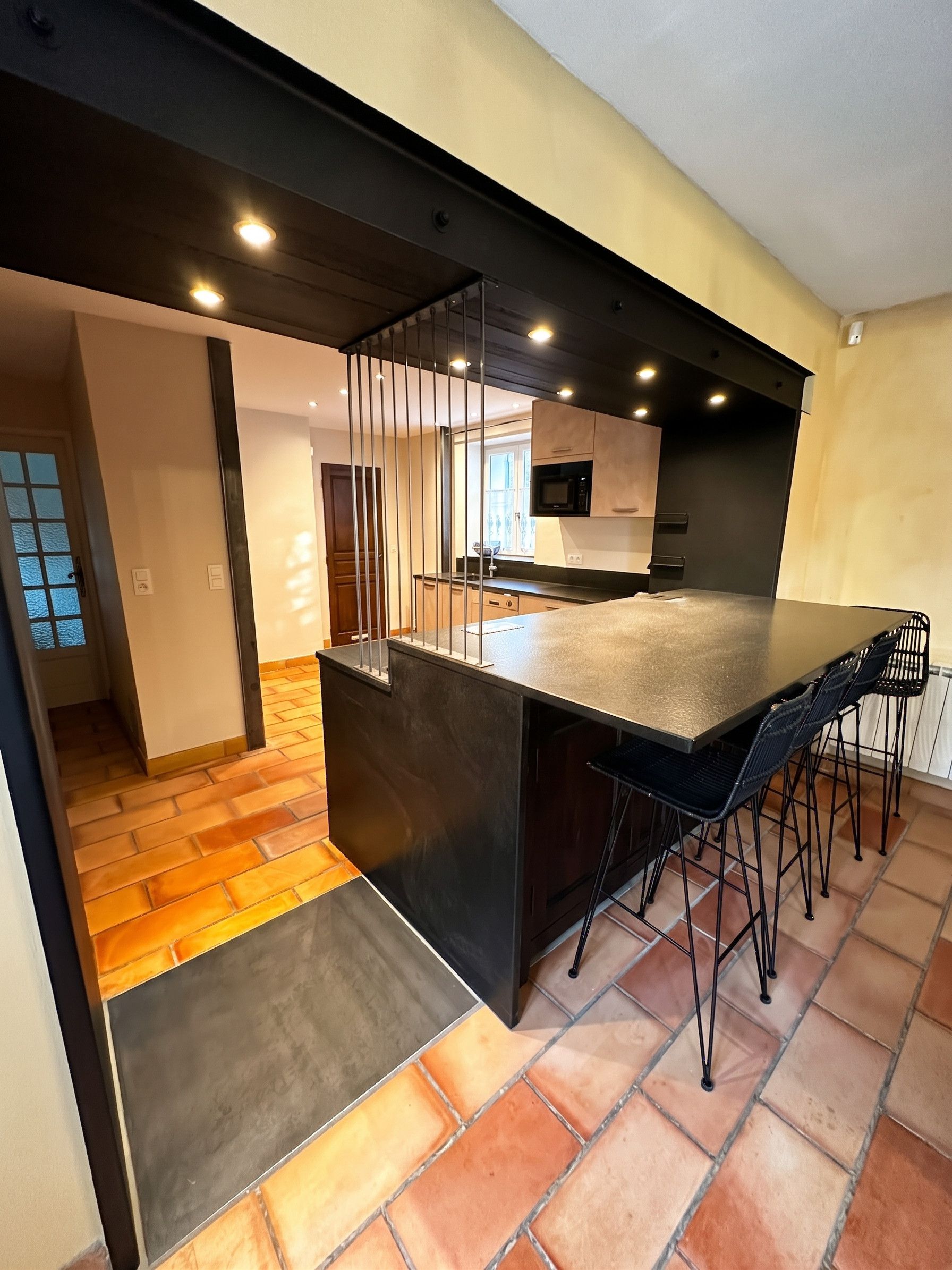 Una cocina moderna con una isla central, taburetes de bar y vista al área de comedor.