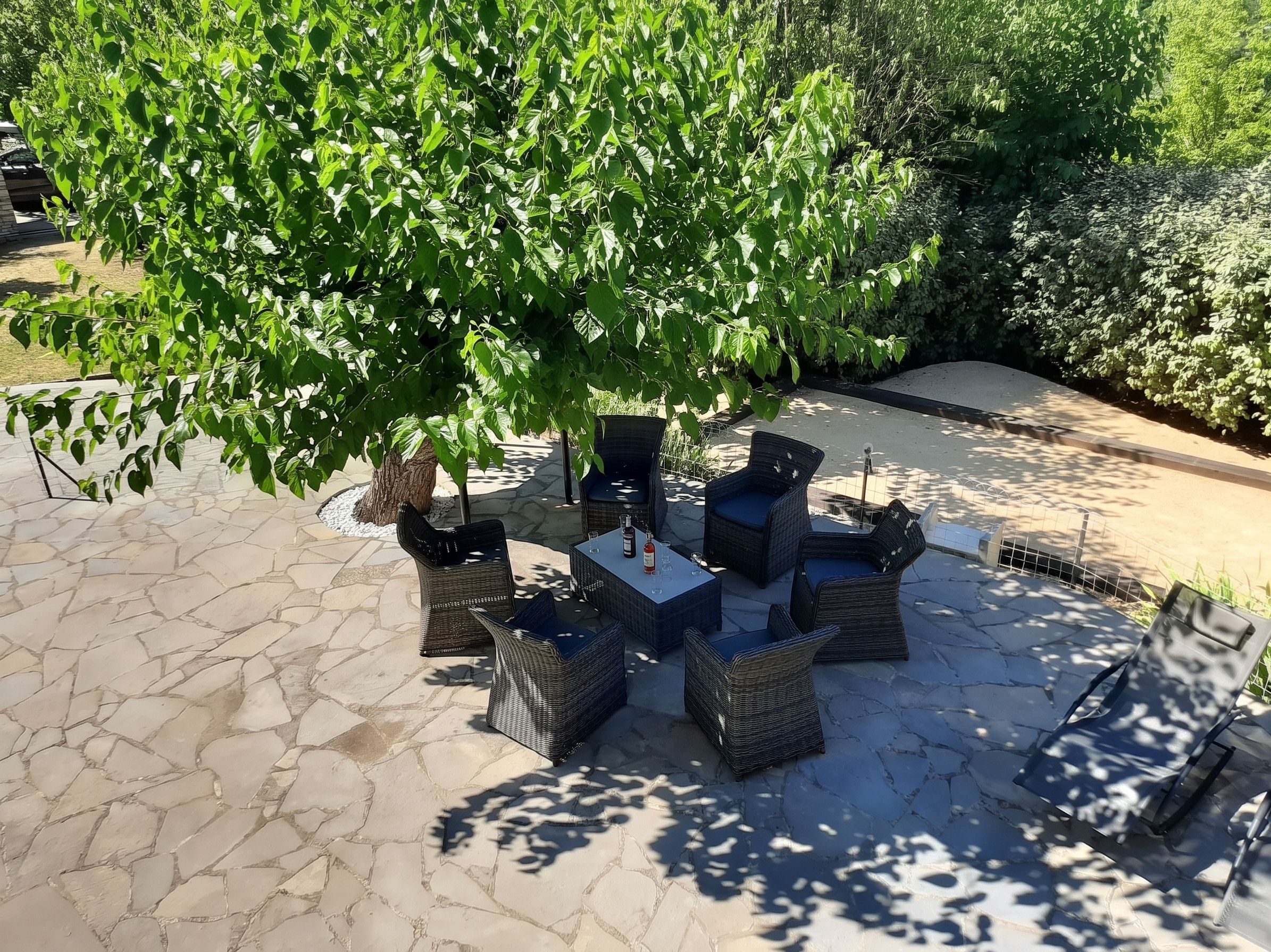 Un'area salotto all'aperto con mobili in vimini e un albero che offre ombra.