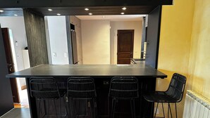 Une cuisine dotée d’un grand îlot central, de quatre tabourets de bar et donnant sur la pièce adjacente.