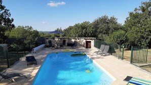 Une piscine rectangulaire à l’eau d’un bleu cristallin, entourée de chaises longues et d’un mur en pierre.