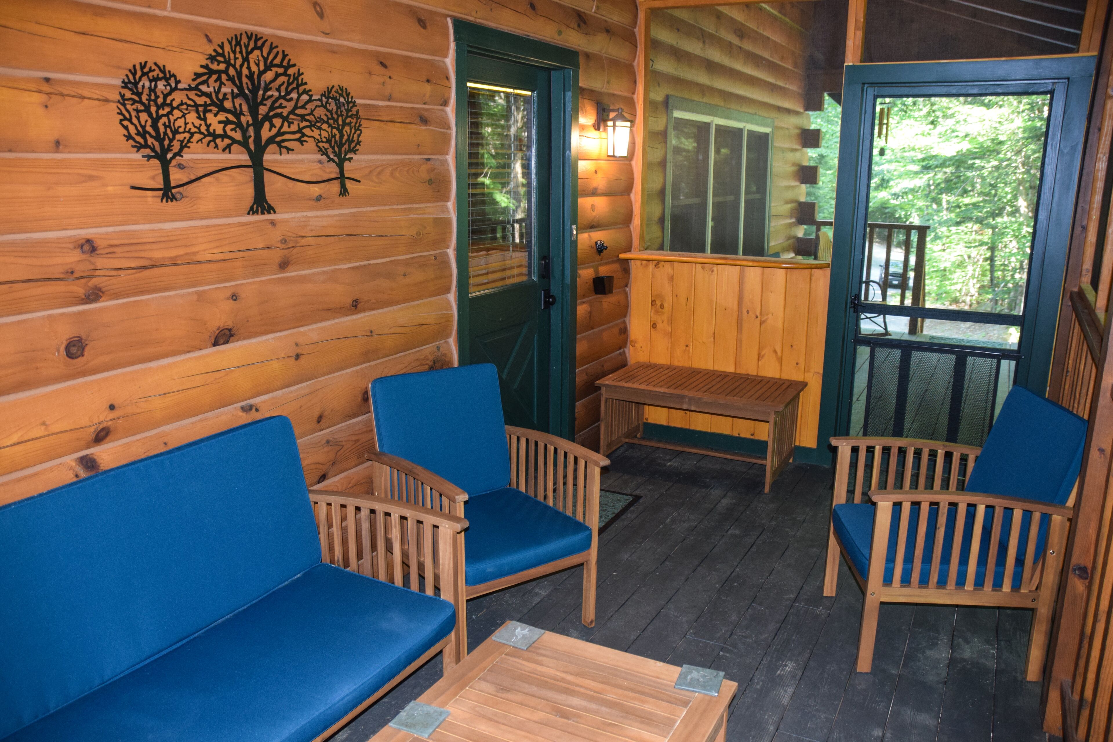 Eine Holzhütte mit Veranda, zwei blaue Sitzgelegenheiten, einem Holztisch und einer Tür mit Baumaufkleber.
