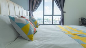 A hotel room with a large bed, colorful pillows, and a view of a cityscape through a window with curtains.