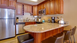 A kitchen with wooden cabinets, a stainless steel refrigerator, granite countertops, and a built-in island with bar seating. - Walk to Copper Mountain Lifts: Mtn-View Condo (Copper Mountain)
