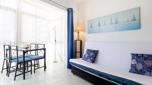 Una sala moderna con un sofá, una mesa de comedor con sillas y un cuadro de barcos de vela en la pared.