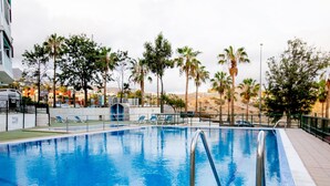 Una piscina con agua cristalina azul, rodeada de palmeras y una valla blanca.