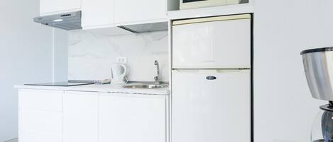 A modern kitchen with white cabinetry, a built-in microwave, a stainless steel sink, and a coffee maker.