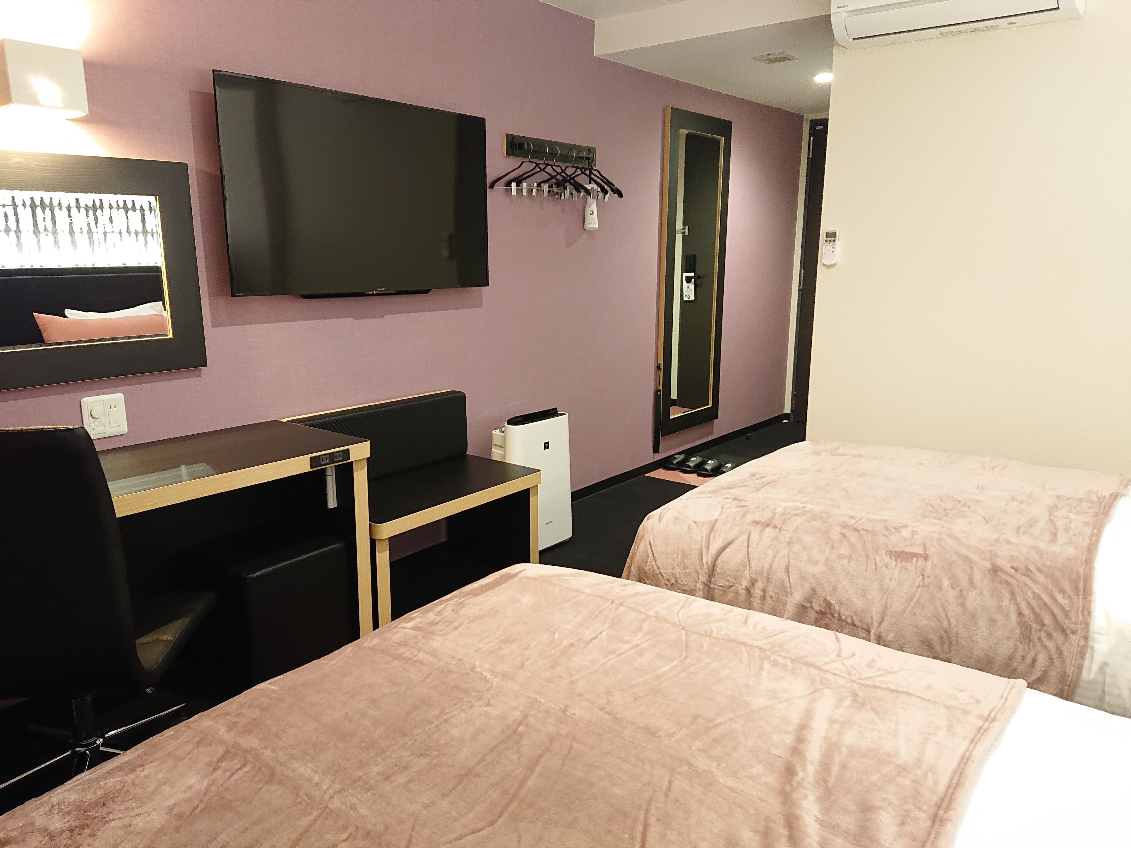 A hotel room with two beds, a desk, a chair, a TV, a mirror, and a coat rack.