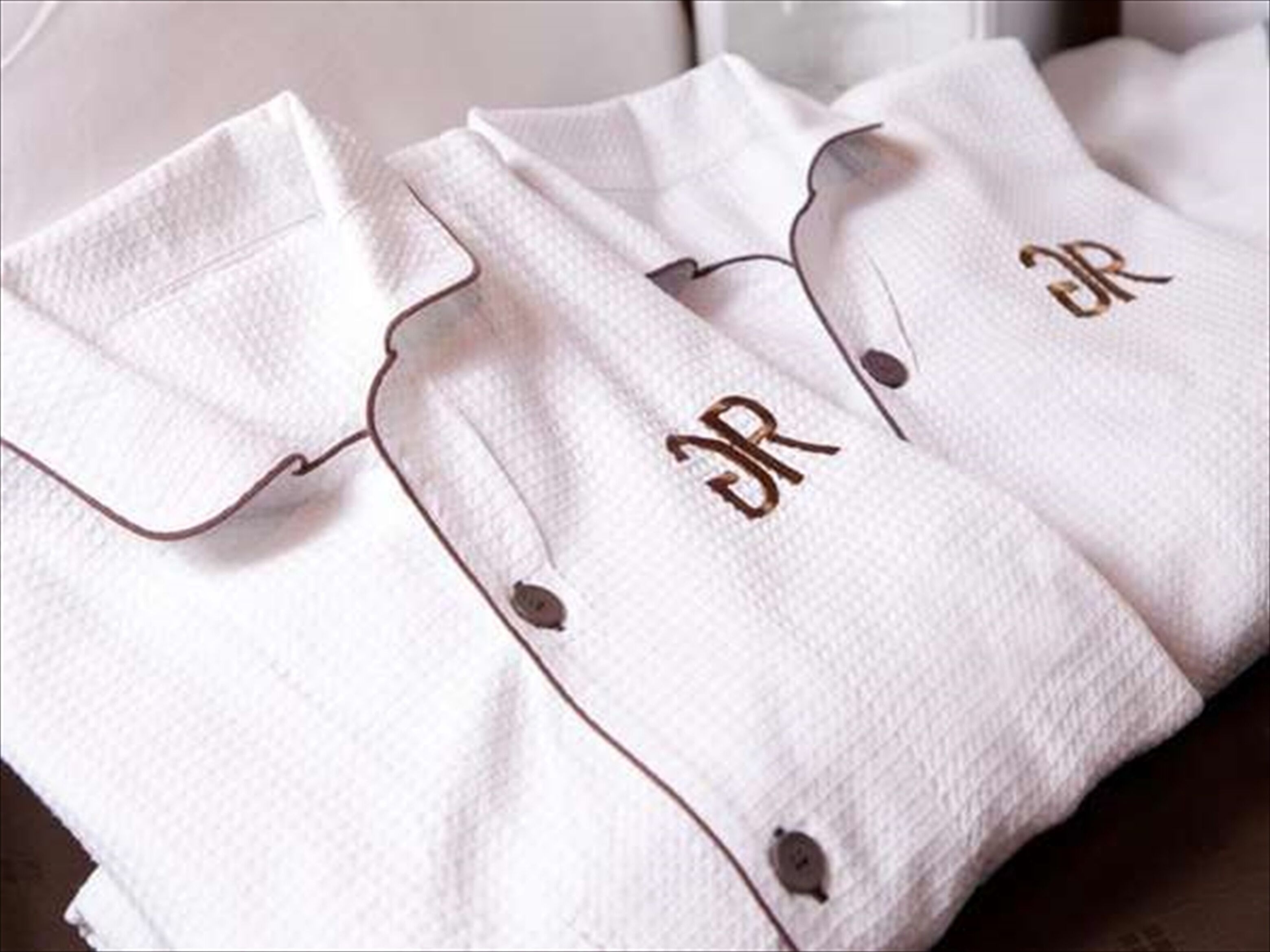 Una camisa blanca con un botón y letras bordadas.