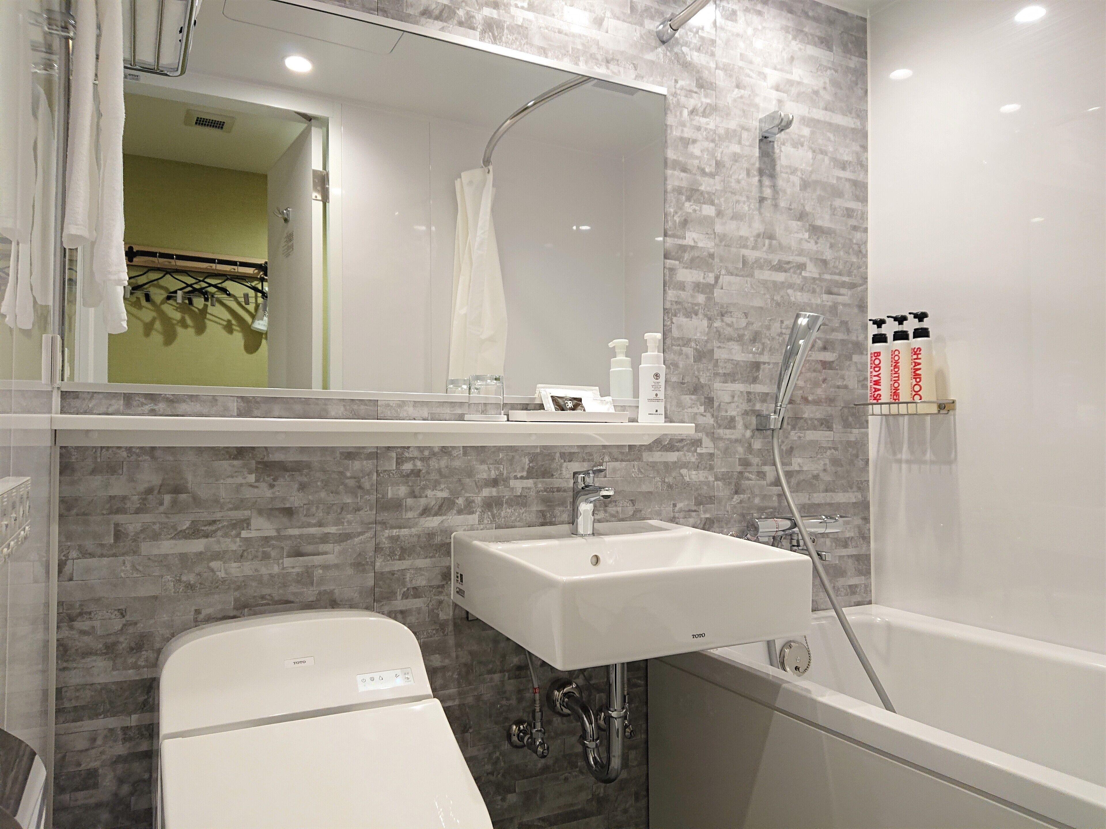 A modern bathroom with a white sink, a bathtub, and a shower. There are toiletries on the sink and a towel rack.