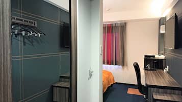 A hotel room with a bed, a desk, a chair, a TV, and a coat rack.